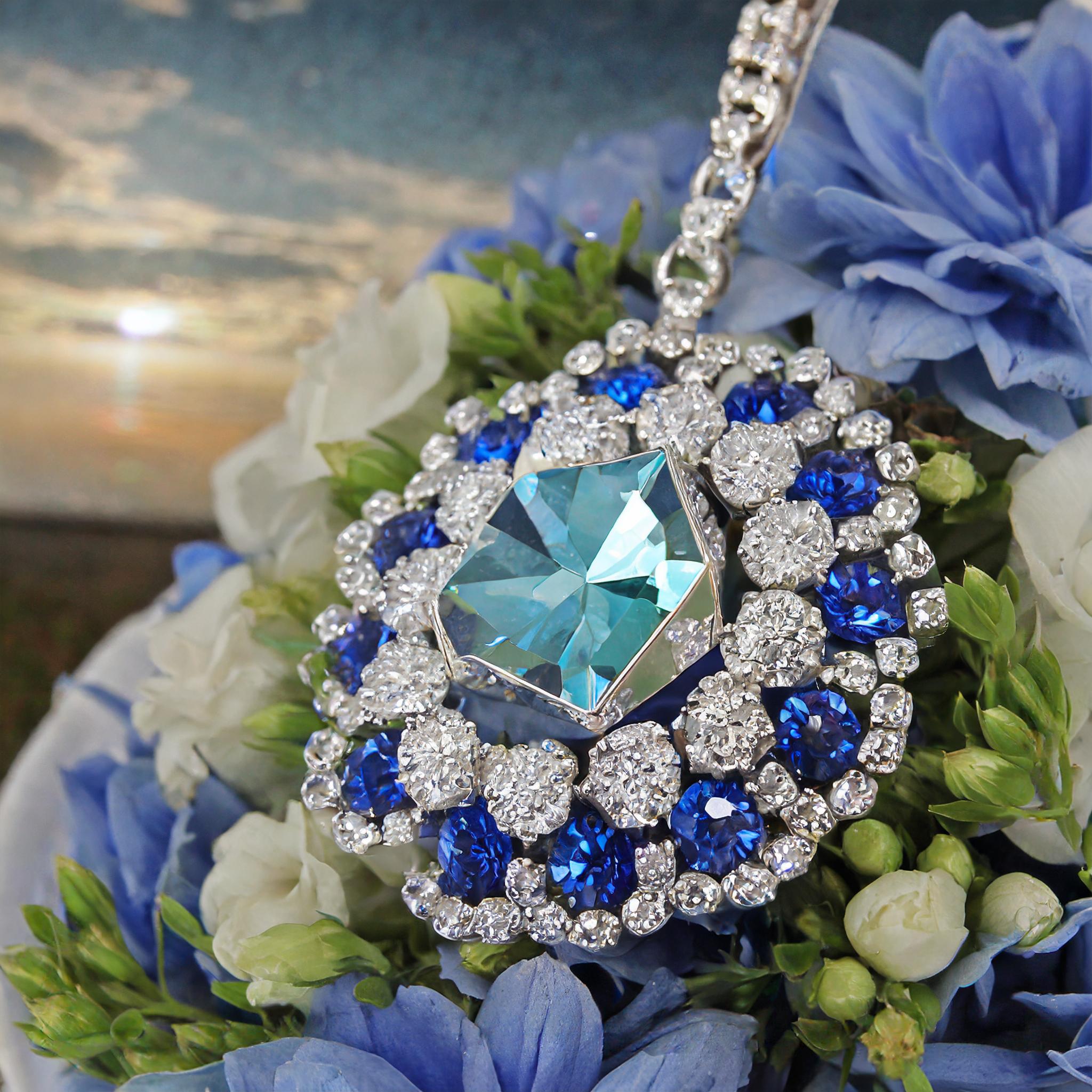 Firefly emeraude bague diamant 60633 c'est un collier qui est présenter sur des fleurs. le pendentif a des diamant blanc et bleu. Au centre du pendentif le diamant est bleu clair.